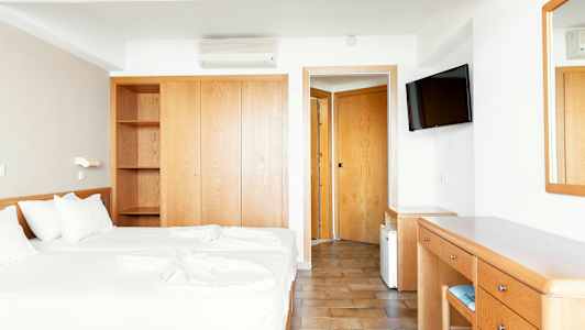 Hotellihuone, jossa on kaksi erillistä vuodetta, vaatekaappi, kirjoituspöytä ja peili. (Tekoälyn luoma teksti)