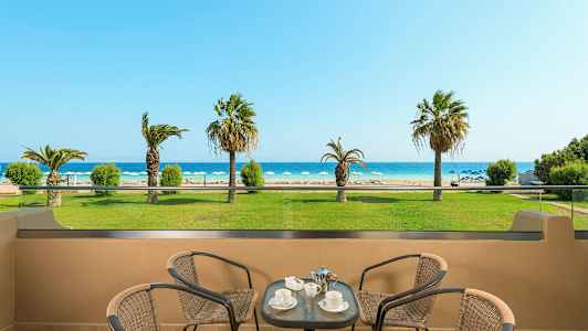 Näkymä terassilta rannalle, jossa on aurinkotuoleja ja palmupuita, etualalla pöytä ja tuolit. (Tekoälyn luoma teksti)