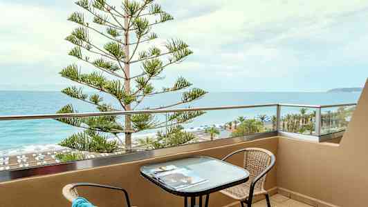 Parveke, jolta avautuu näkymä merelle ja rannalle, pöytä ja tuolit. (Tekoälyn luoma teksti)