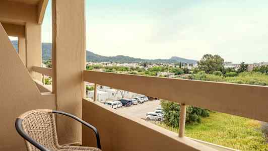 Parveke, jossa on tuoli ja näkymä parkkipaikalle sekä vehreyttä ja vuoria kaukaisuudessa. (Tekoälyn luoma teksti)