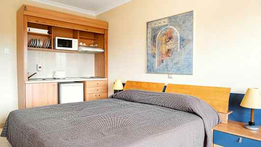 Huone, jossa on sänky, pieni keittiö ja seinämaalaus. (Tekoälyn luoma teksti)