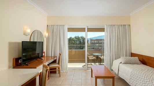 Hotellihuone, jossa on televisio kirjoituspöydällä, kaksi erillistä vuodetta ja parveke ulkokalusteilla. (Tekoälyn luoma teksti)