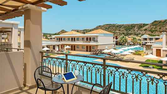 Näkymä parvekkeelta uima-altaalle ja hotellirakennuksiin, joissa on aurinkotuoleja ja aurinkovarjoja. (Tekoälyn luoma teksti)