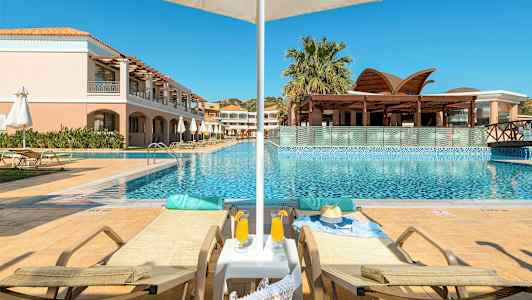 Kaksi aurinkotuolia uima-altaan äärellä, varjo ja rakennus taustalla. (Tekoälyn luoma teksti)