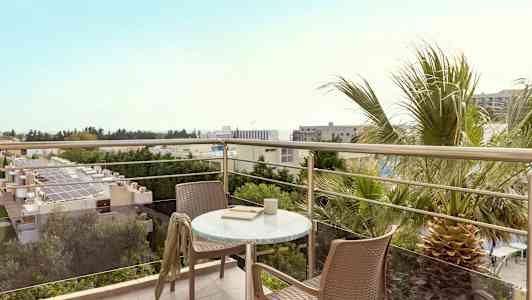 Näkymä parvekkeelta, jossa on pöytä ja kaksi tuolia, ympärillä on puita ja rakennuksia. (Tekoälyn luoma teksti)