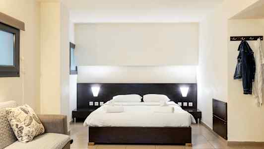 Hotellihuone, jossa on parivuode, sohva ja vaatekoukkuja. (Tekoälyn luoma teksti)