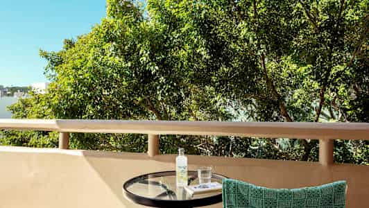 Parvekkeen kuva pyöreän pöydän kanssa, pyyhe roikkuu tuolin selkänojalla ja taustalla on puita. (Tekoälyn luoma teksti)