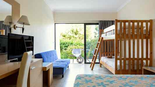 Hotellihuone, jossa on kerrossänky, sininen sohva, työpöytä, televisio ja parveke näkymällä vehreyteen. (Tekoälyn luoma teksti)