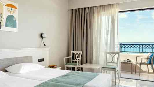 Hotellihuone, jossa parivuode, kaksi tuolia ja pöytä ikkunan äärellä, merinäköala. (Tekoälyn luoma teksti)