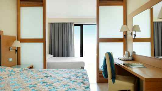 Hotellihuone, jossa on parisänky, kirjoituspöytä ja näkymä lasi-ikkunan läpi. (Tekoälyn luoma teksti)