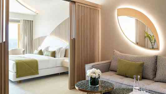 Moderni hotellihuone, jossa on sohva ja sänky, sisustettu luonnollisilla väreillä ja puuyksityiskohdilla. (Tekoälyn luoma teksti)