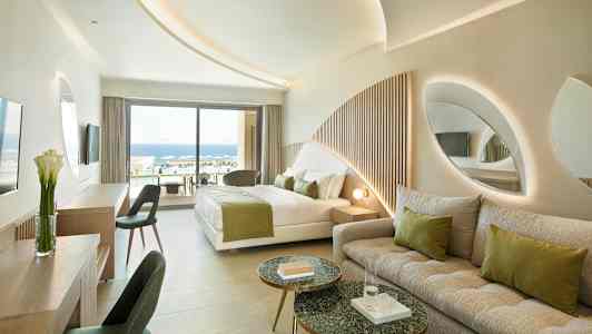 Moderni hotellihuone, jossa sänky, sohva ja näkymä uima-altaalle ja merelle. (Tekoälyn luoma teksti)