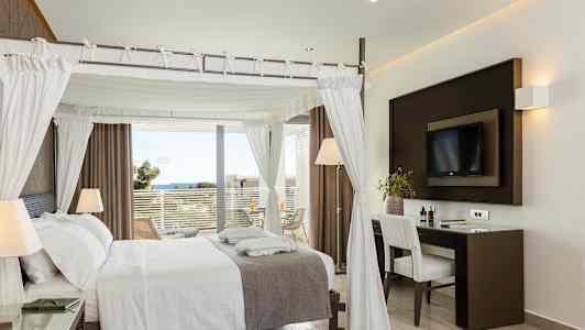 Tyylikäs hotellihuone, jossa on pylvässänky, työpöytä ja parvekkeelta avautuva merinäköala. (Tekoälyn luoma teksti)