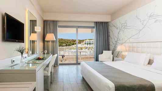 Nykyaikainen hotellihuone, jossa on suuri sänky, työpöytä, televisio ja parveke näkymällä. (Tekoälyn luoma teksti)