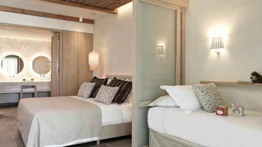 Moderni hotellihuone, jossa on kaksi sänkyä, koristeellinen valaistus ja näkyvä kylpyhuoneosa kahdella peilillä. (Tekoälyn luoma teksti)