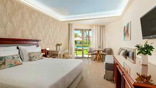 Hotellihuone, jossa parivuode, kirjoituspöytä ja oleskelutila. Näkymä puutarhaan. (Tekoälyn luoma teksti)