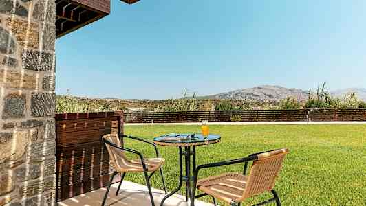 Terassi, jossa pöytä ja kaksi tuolia, nurmikko ja vuoret taustalla. (Tekoälyn luoma teksti)