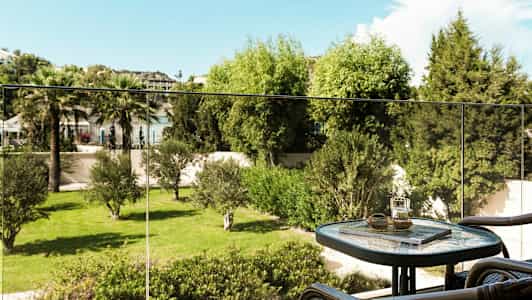 Parveke, jossa on pöytä ja tuoleja sekä näkymä vihreään puutarhaan. (Tekoälyn luoma teksti)