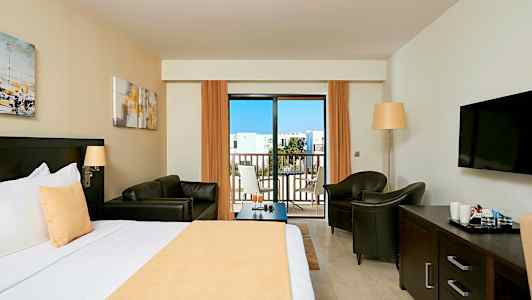 Hotellihuone, jossa sänky, oleskelualue, televisio ja parveke. (Tekoälyn luoma teksti)