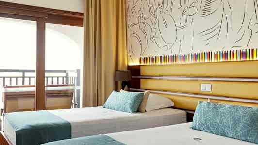 Hotellihuone, jossa on kaksi yhden hengen vuodetta turkooseilla koristeilla ja taustalla seinällä taiteellinen koristelu sekä pieni lamppu. (Tekoälyn luoma teksti)