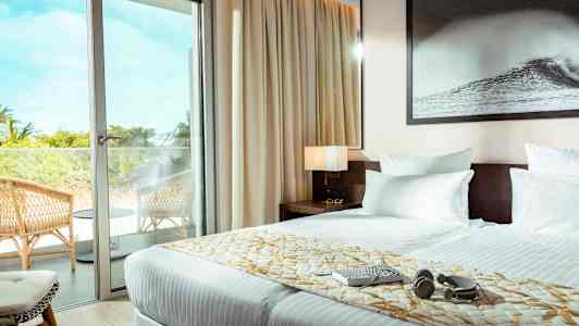 Hotellihuone, jossa on parivuode ja lasiovi, joka johtaa parvekkeelle, jossa on tuoleja. (Tekoälyn luoma teksti)