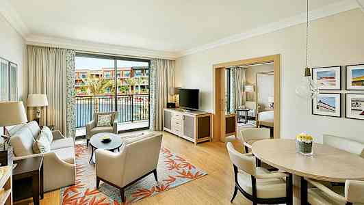 Hotellihuone, jossa on olohuone, ruokapöytä ja parveke, joka avautuu ulkoaltaalle. (Tekoälyn luoma teksti)