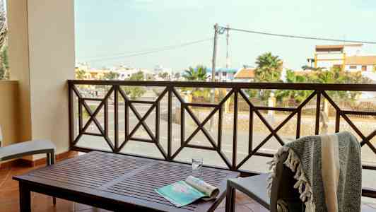 Parveke, jossa pöytä ja tuolit, näkymä kadulle ja rakennuksiin. (Tekoälyn luoma teksti)