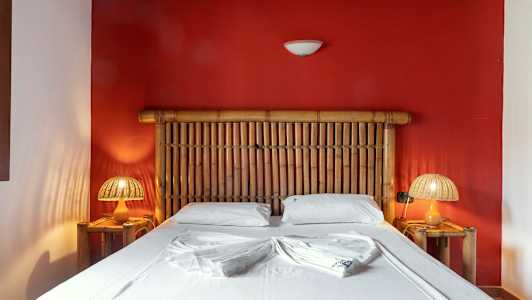 Makuuhuone, jossa bambusänky punaisen seinän edessä (Tekoälyn luoma teksti)