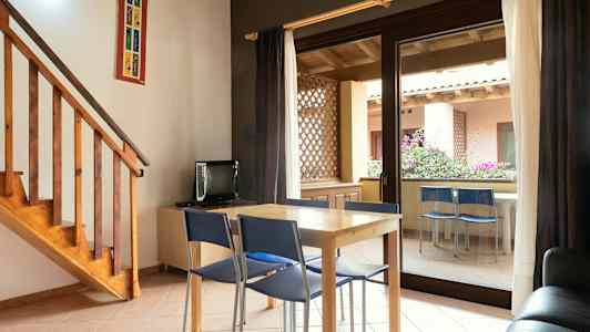 Huone, jossa on pöytä ja tuolit lasioven edessä ja joka johtaa terassille. (Tekoälyn luoma teksti)