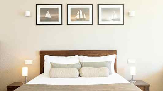 Makuuhuone, jossa on sänky, kaksi lamppua yöpöydillä ja kolme taulua seinällä. (Tekoälyn luoma teksti)