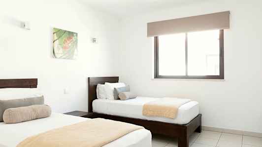 Kaksi erillistä sänkyä valoisassa makuuhuoneessa, jossa on ikkuna ja seinäkoriste. (Tekoälyn luoma teksti)