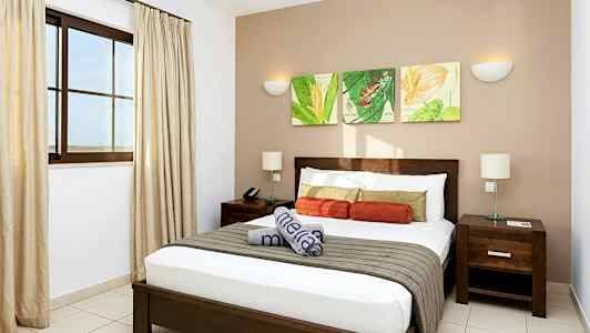 Moderni hotellihuone, jossa on parisänky, yöpöydät ja koristeellinen seinätaide. (Tekoälyn luoma teksti)