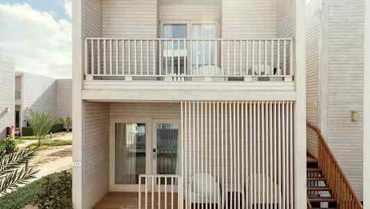 Kaksikerroksinen rakennus puuparvekkeilla, ympäröitynä vihreällä kasvillisuudella. (Tekoälyn luoma teksti)