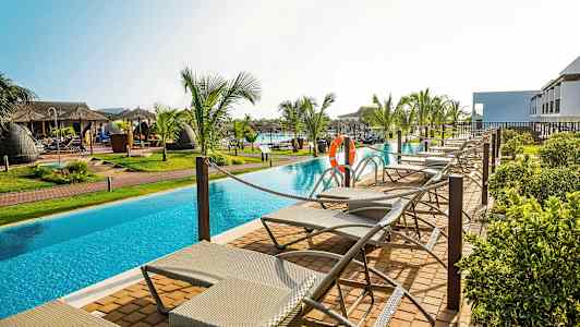 Aurinkotuoleja uima-altaan äärellä palmujen ympäröiminä. (Tekoälyn luoma teksti)