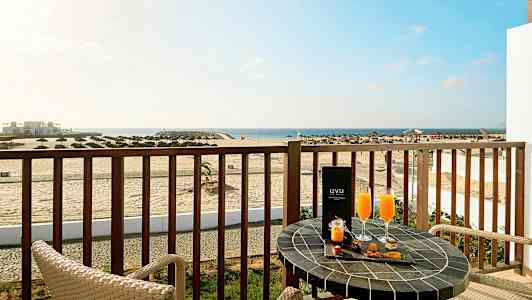 Parveke, josta avautuu näkymä rannalle ja merelle, kaksi tuolia ja pöytä, jolla on juomia ja välipaloja. (Tekoälyn luoma teksti)