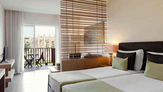 Hotellihuone, jossa kaksi yhden hengen vuodetta, oleskelualue väliseinällä ja terassi näkymällä. (Tekoälyn luoma teksti)