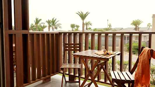 Parveke, jossa ulkokalusteita ja näkymä palmujen ja muiden rakennusten yli. (Tekoälyn luoma teksti)