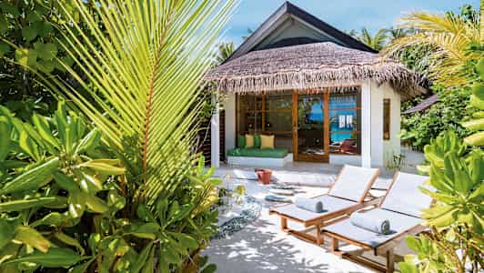 Aurinkotuoleja ja trooppisia kasveja bungalowin edessä, merinäköalalla. (Tekoälyn luoma teksti)