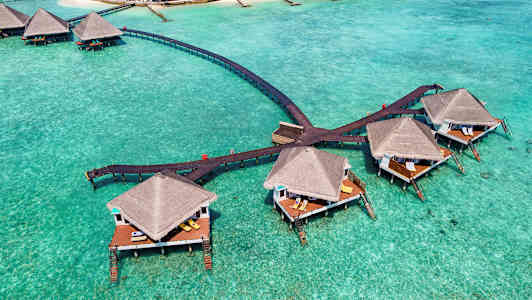 Bungalowit pylväillä turkoosin veden yllä, yhdistettynä puusilloilla. (Tekoälyn luoma teksti)