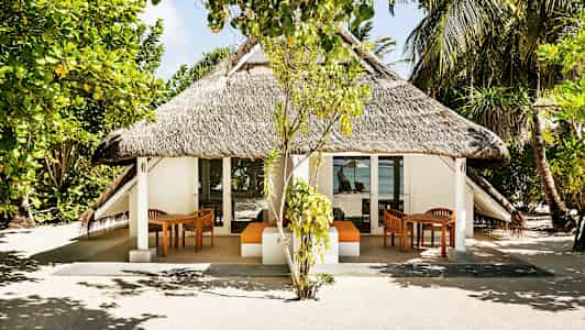 Ruohokattoinen bungalow, jota ympäröivät puut ja kasvillisuus, taustalla merinäköala. (Tekoälyn luoma teksti)