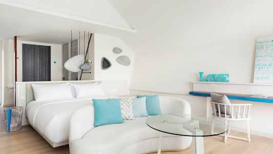 Moderni ja valoisa hotellihuone, jossa on suuri sänky, sohvaryhmä lasipöydällä ja työalue. (Tekoälyn luoma teksti)