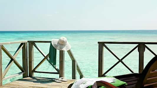 Puisella terassilla meren äärellä on valkoinen aurinkohattu ja vihreä vaate roikkuvat kaiteesta. (Tekoälyn luoma teksti)