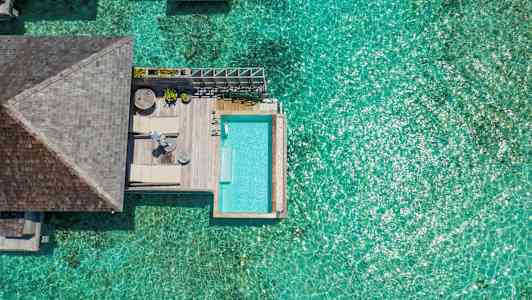 Ylhäältä otettu kuva aurinkoisesta vesivillasta, jossa on uima-allas ja kirkas sininen meri. (Tekoälyn luoma teksti)