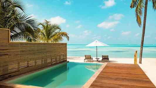 Uima-allas puuterassin vieressä, josta avautuu näkymä rannalle, jossa on aurinkovarjo ja aurinkotuoleja. (Tekoälyn luoma teksti)