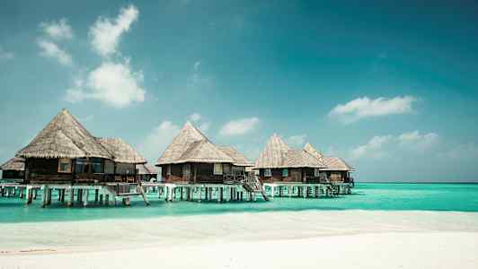 Bungalowit pylväiden päällä sinisen veden äärellä rannalla. (Tekoälyn luoma teksti)