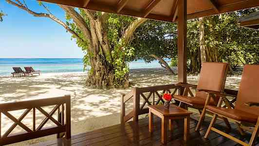 Näkymä verannalta, jossa on tuoleja ja pöytä, rannalle aurinkotuoleineen ja merelle. (Tekoälyn luoma teksti)