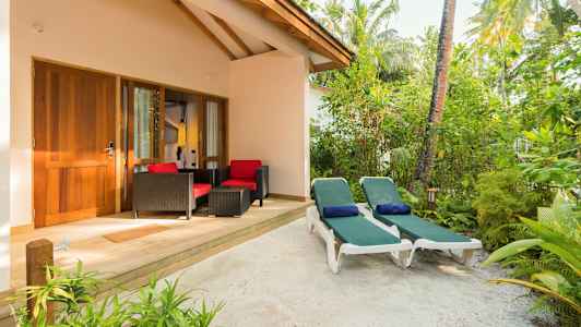 Terassi, jossa kaksi aurinkotuolia ja istuinryhmä rakennuksen edessä vihreän ympäröimänä. (Tekoälyn luoma teksti)