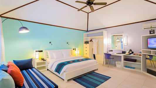 Vaalea hotellihuone, jossa on parivuode, värikäs sisustus ja istuma-alue. (Tekoälyn luoma teksti)