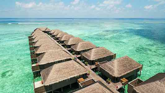 Kuvassa näkyy rivi vesibungaloweja, joissa on olkikatot ja jotka on rakennettu paalujen varaan turkoosin laguunin ylle. (Tekoälyn luoma teksti)