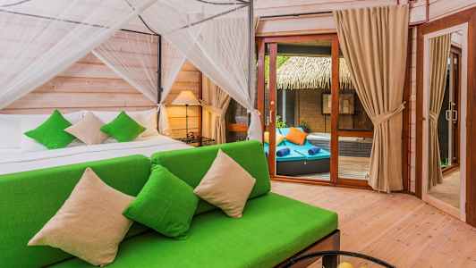 Makuuhuone, jossa on vihreä sohva ja vuode vihreillä koristetyynyillä. Oikealla on lasiovi, joka johtaa terassille, jossa on aurinkotuoleja. (Tekoälyn luoma teksti)